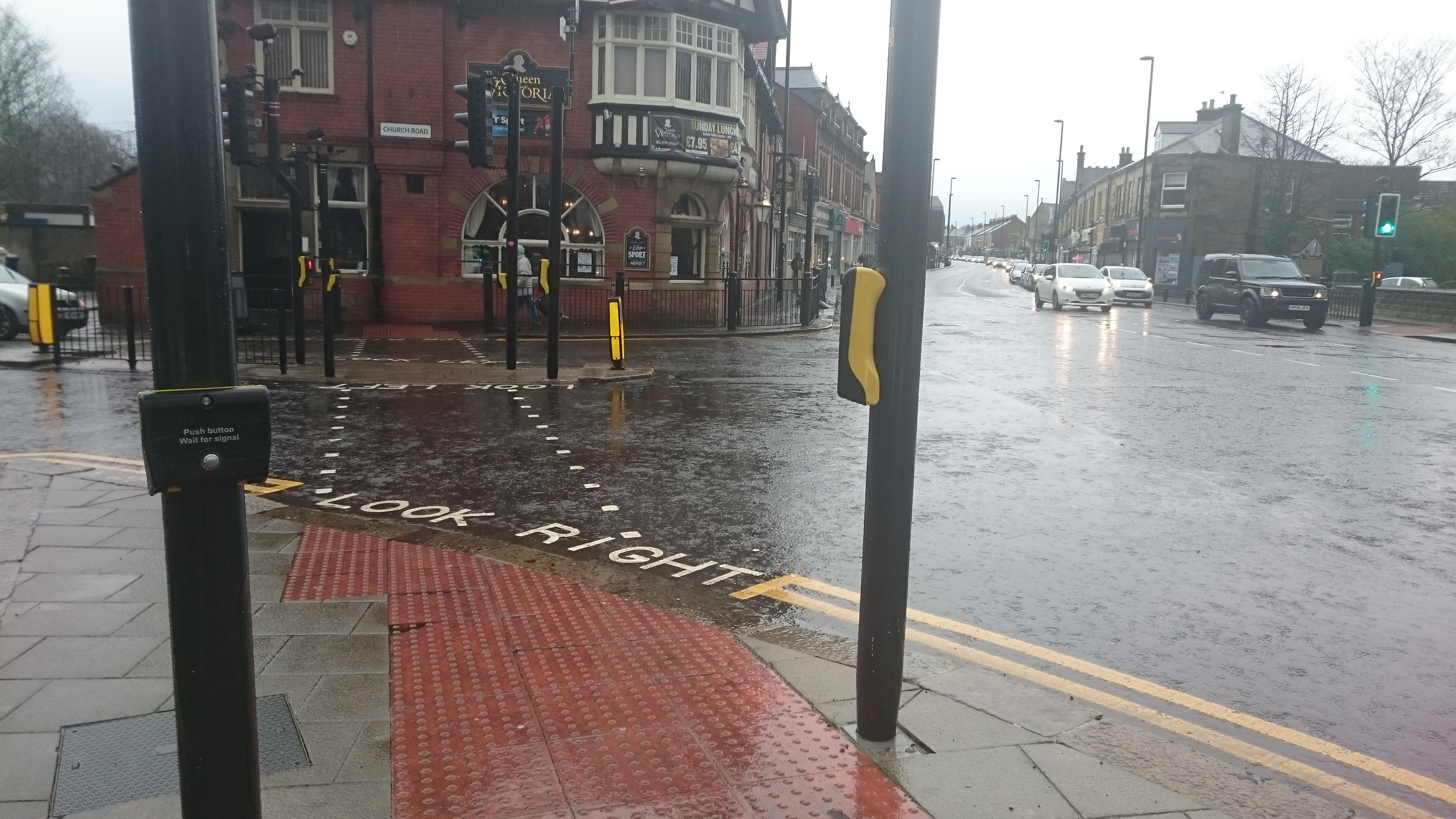 image of crossing across church road heading towards the Queen Victoria pub. Showing the tactile paving and the curved edge of the pavment. Look right is painted on the road.